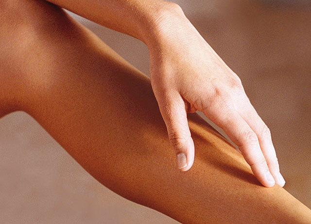 Glatt rasiertes Bein einer Frau, mit einer darauf liegenden Hand